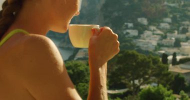 Terasta sabah kapuçinosunu yudumlayan bir kadın. Capri İtalya 'nın panoramik manzarası ve sahil şeridi..