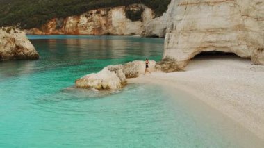 Beyaz kayalıkların ve turkuaz deniz suyunun yakınındaki tenha bir koy sahilinde yürüyen bir kadın..