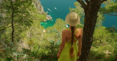 Uçurumun kenarındaki çam ağaçlarının arasında dikilen kadın Capri İtalya 'nın turkuaz denizine doğru bakıyor..