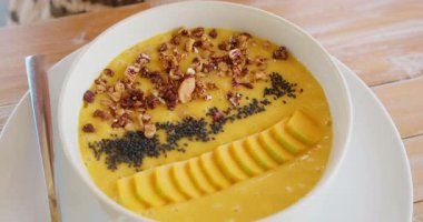 Dilimlenmiş meyve ve tahıl taneleriyle kaplı mango tropikal meyve suyu kasesi..