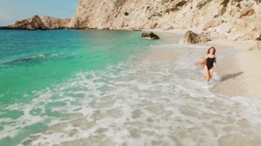 Yazın güneşli çakıl taşlı plajda deniz dalgaları boyunca koşan kadın Petani Kefalonia.