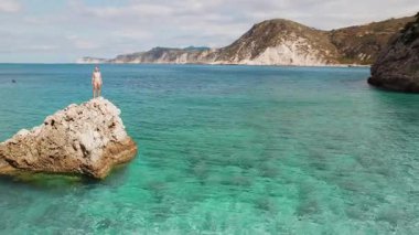 Kefalonia 'daki sahil kayalıklarının yakınındaki turkuaz denizin üzerinde duran kadın..