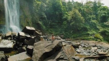 Tropik ormanlarla çevrili şelale yakınlarındaki büyük kayalıklarda yürüyen bir kadın..