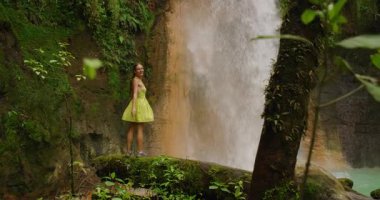 Kosta Rika 'nın güçlü şelalesinin yanında duran kadın seyahat sırasında gülümsüyor.