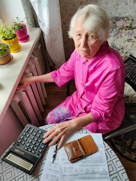 The senior woman holding gas bill in front of heating radiator. Payment for heating in winter.