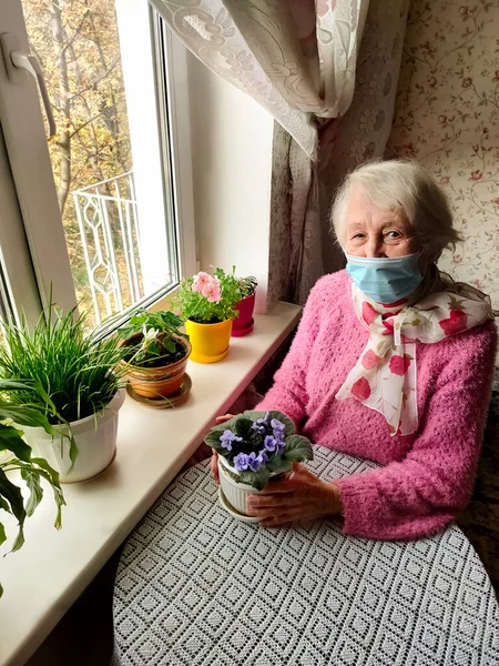 第二波 Covid 安全和流行病概念 戴着防护医疗面罩的老年孤寡老人坐在家中靠窗的地方 以防止感染病毒 — 图库照片