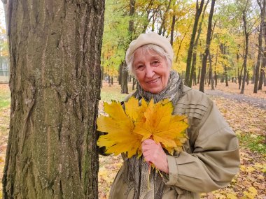 Gri saçlı, gülümseyen yaşlı kadın sonbahar parkında. Mutlu yaşlılık, doğa yürüyüşü, olumlu duygular..