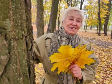 Gri saçlı, gülümseyen yaşlı kadın sonbahar parkında. Mutlu yaşlılık, doğa yürüyüşü, olumlu duygular..