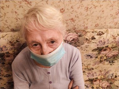 İkinci dalga. Covid-19, sağlık, güvenlik ve salgın konsepti - koruyucu maske takan yaşlı, yalnız bir kadın virüsten korunmak için evde oturuyor.