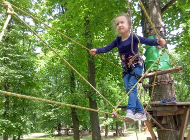 Yeşil ağaçlara karşı macera halat parkına tırmanan kız.