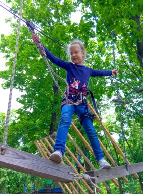 Yeşil ağaçlara karşı macera halat parkına tırmanan kız.