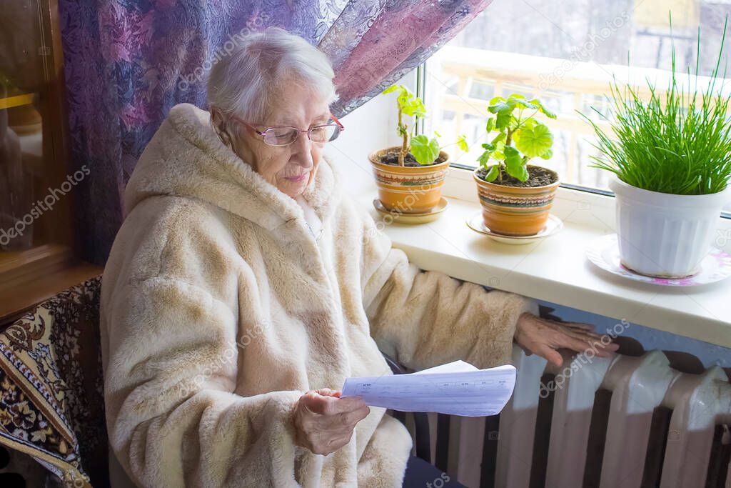 The senior woman holding gas bill in front of heating radiator. Payment for heating in winter.