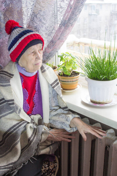 The senior woman sitting in front of heating radiator. Payment for heating in winter.