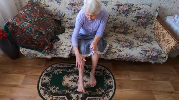 Senior vrouw aanbrengen crème op haar benen zitten op de bank — Stockvideo