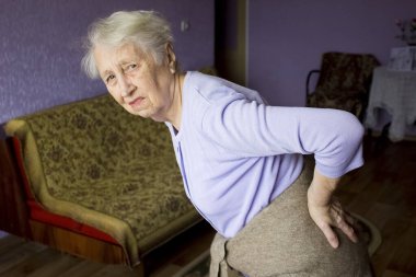 Yaşlı 75 'li yaşlarda, sırt ağrısı ve sırt ağrısını azaltmak için sırt masajı yapan yaşlı bir kadın. Yaşlıların hastalıkları, siyatik sinir hasarı konsepti