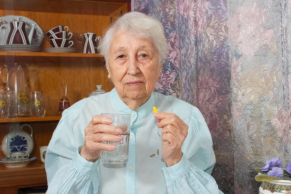 Старша Сіроока Жінка Приймає Таблетки Тримаючи Склянку Води Сидячи Вдома — стокове фото