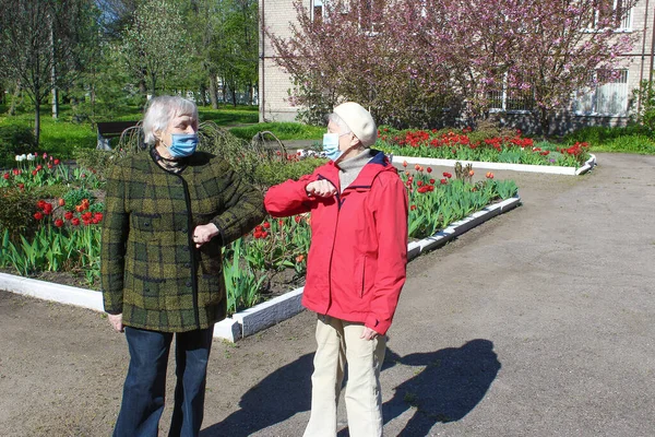 Dois idosos usando máscaras faciais e luvas saudação com sinal de mão, ao ar livre — Fotografia de Stock