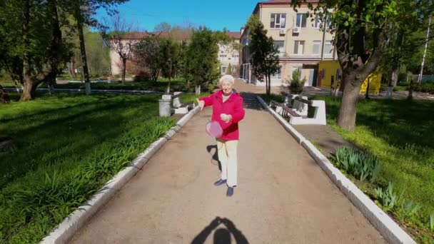 Seniorkvinne på engen som spiller badminton i parken. – stockvideo