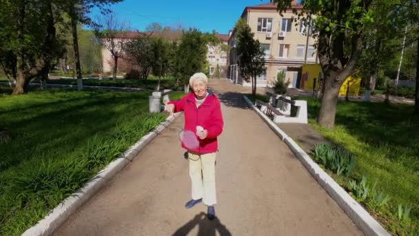 Seniorkvinne på engen som spiller badminton i parken. – stockvideo