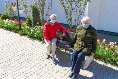 Sosyal uzaklıktaki üzgün yaşlı kadınlar parkta oturuyorlar. Covid-19, sağlık, güvenlik ve salgın konsepti