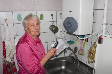 Evdeki üzgün yaşlı kadın gaz faturasını inceliyor. Hesapları kontrol ederken stres altında..