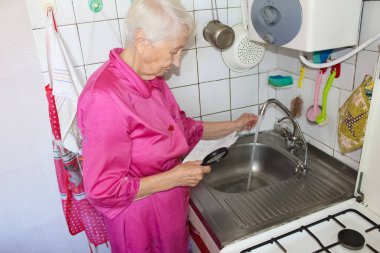 Dehşete düşmüş yaşlı kadın su sayacını kontrol ediyor. Su tüketimi ve pahalı su konsepti.