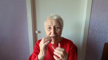 Diş konsepti. 90 yaşında yaşlı bir kadın takma diş takıyor. Yaşlı kadın gri arka planda diş protezi kullanıyor. Stüdyoya yapay çene takan eski bir hasta. Esnek naylon takma diş.