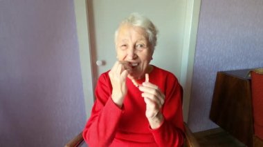 Diş konsepti. 90 yaşında yaşlı bir kadın takma diş takıyor. Yaşlı kadın gri arka planda diş protezi kullanıyor. Stüdyoya yapay çene takan eski bir hasta. Esnek naylon takma diş.