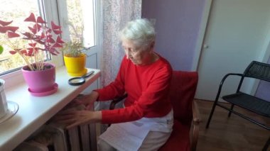 Gaz faturasını kaloriferin önünde tutan yaşlı kadın. Kışın ısıtma için ödeme.