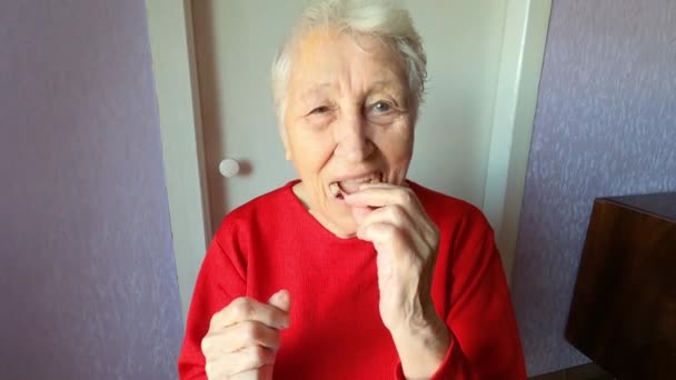 歯の概念 90歳の高齢女性は入れ歯を挿入します 灰色の背景に歯科補綴物を使用したシニア女性灰色の髪 古い患者はスタジオで人工顎を装着 柔軟なナイロンデュエンス — ストック動画