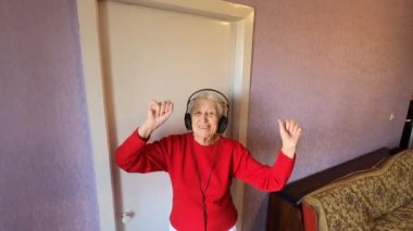 Mutlu, komik, son sınıf öğrencisi, kulaklık takan, evde cep telefonuyla dans eden bir kadın.