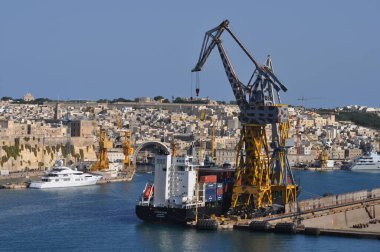 Valletta, Malta - September 24, 2025: Cargo cranes and large ship atlantic silver docked near fortifications and boats in the harbor.
