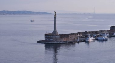 Sicilya ve İtalya arasındaki Messina Boğazı. Madonna della Lettera 'nın altın heykeli ve limana girişi olan Messina kasabasından görüntü. Arka planda Calabria kıyı şeridi