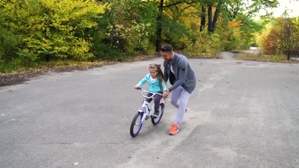 Любящий отец учит дочь кататься на велосипеде в парке — стоковое видео