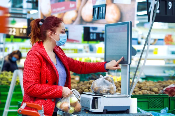 Markette salgın sırasında sebze tartan genç bir kadın.