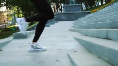 Spor ayakkabılı bir kadın şehirde merdivenlerde koşuyor.