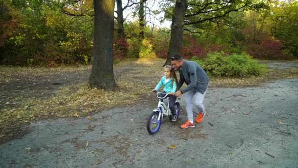 Padre apoyando a su hijita mientras monta en bicicleta — Vídeos de Stock