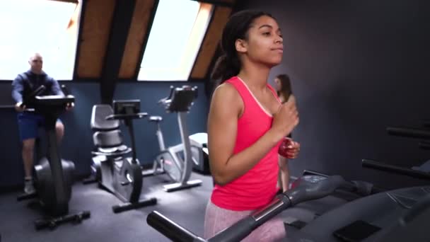 Africká Američanka běží na běžeckém pásu v přeplněné tělocvičně — Stock video
