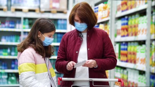 Ibu dan anak bertopeng membaca daftar belanja di supermarket — Stok Video
