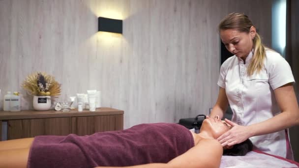 Kosmetyk robi masaż twarzy dla kobiety w spa wellness — Wideo stockowe