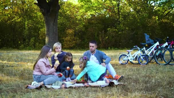Счастливая семья ест фрукты и закуски после езды на велосипеде на природе — стоковое видео