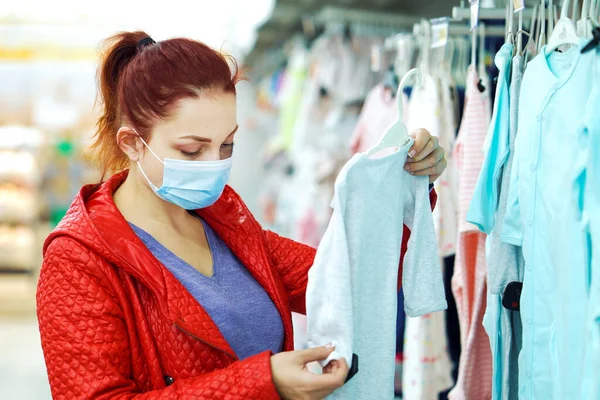 Maskeli kadın salgın sırasında alışveriş merkezinden çocuk kıyafeti alıyor.