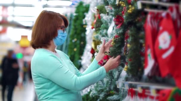 Maskeli kadın süpermarketten Noel çelengi alıyor. — Stok video