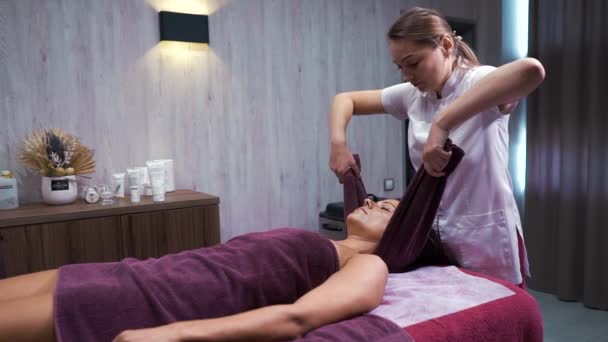 Терапевт с использованием полотенца для массажа шеи женщины-клиента в оздоровительном спа — стоковое видео