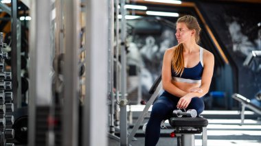 Kadın spor salonunda dambıllarla antrenman yaptıktan sonra dinleniyor.