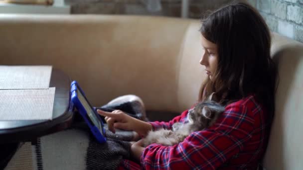 Mädchen im Pyjama kuschelt Katze und schaut Tablet — Stockvideo