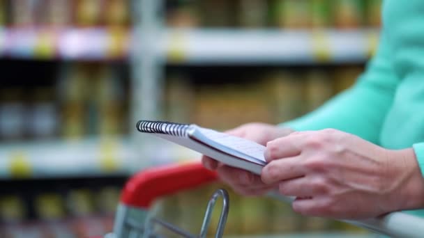 Mãos femininas virando página da lista de compras enquanto no supermercado — Vídeo de Stock