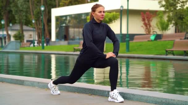 Впишеться жінка займається спортом і розтягує ноги в парку — стокове відео