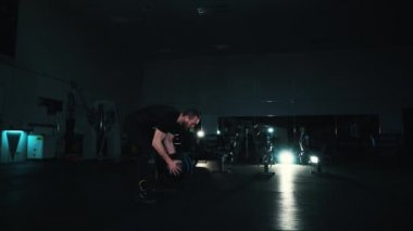 Sporcu, koyu renk spor salonunda ağır topla antrenman yapıyor.
