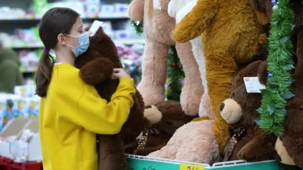 Girl in mask hugging teddy bear in supermarket — Stockvideo